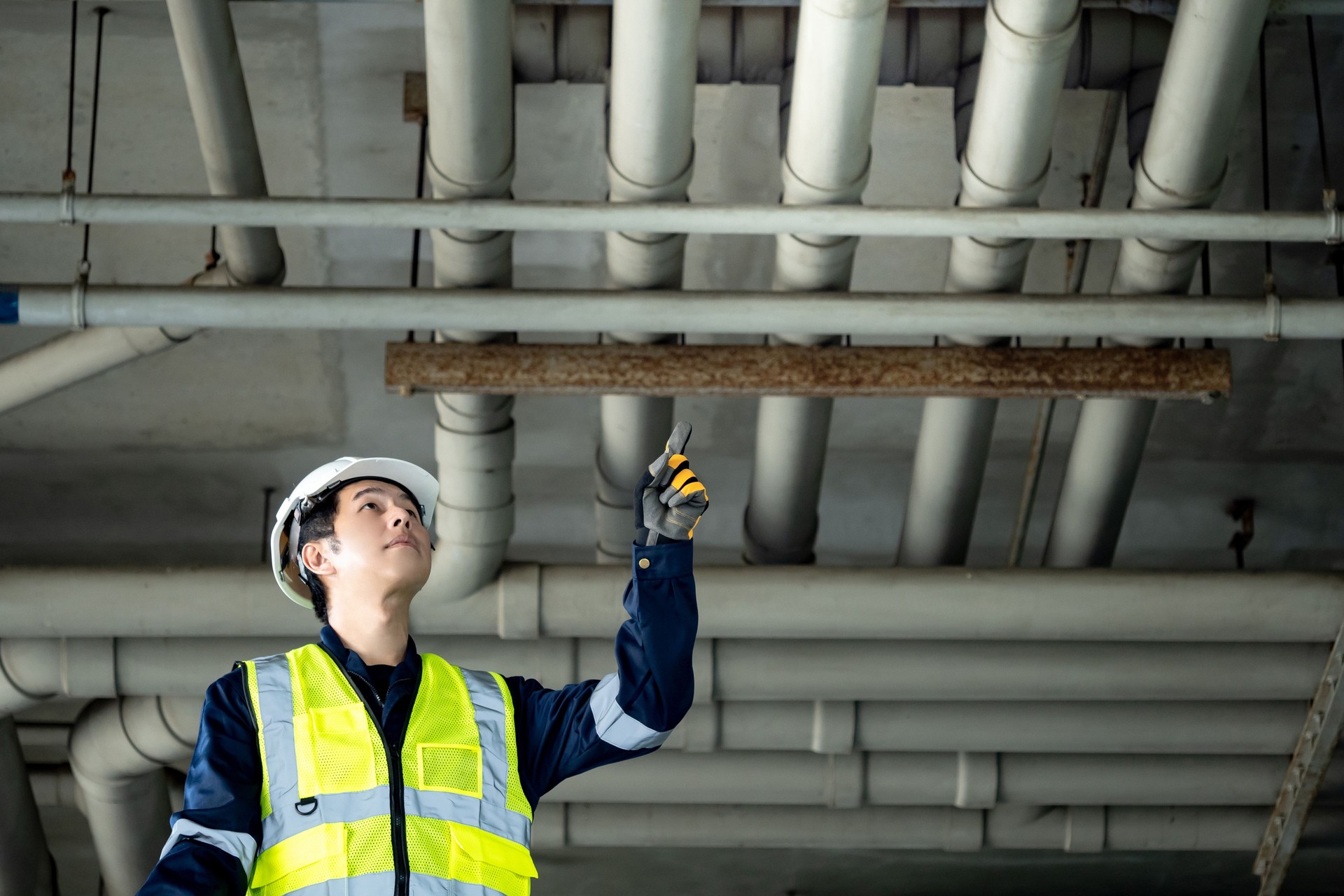 Asian male building inspection engineer pointing at plumber piping system. Construction worker at construction site